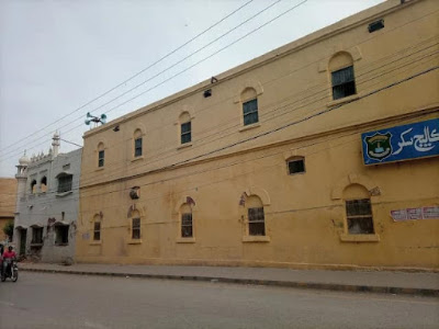 Current View of Madrasa Board Hostel from Minara Road A present-day view of the Madrasa Board Hostel, now part of Agha Nizamuddin Girls College, as seen from Minara Road. The building features traditional architecture with visible signage and surrounding urban elements.