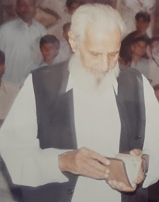 Qadri Sahib Honoring the Winning Team – Football Final Ceremony The late Qadri Sahib presenting an award to the winning team at the football final, wearing a red flower garland and shaking hands with a player in a blue Adidas jersey.