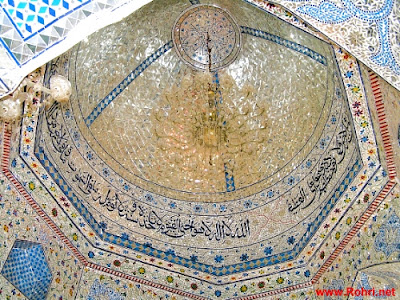 Sacred Reflections – Glass Mosaic Dome with Arabic & Farsi Inscriptions at Jan Allah Shah Shrine Interior dome of Jan Allah Shah shrine in Rohri, Sindh, adorned with mirrored glasswork, floral mosaics, and Arabic calligraphy including "La ilaha illallah Muhammadur Rasul Allah Aliyun Waliullah".
