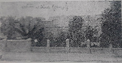 Historic Entrance to the Old Parish Cemetery – Photograph from 1907 Grainy black-and-white photo of a large historic building partially hidden by trees, with a stone fence in the foreground.