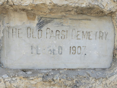 Historic Plaque of the Old Parsi Cemetery – Closed in 1907 Weathered stone plaque embedded in a rough wall, engraved with “THE OLD PARSI CEMETERY CLOSED 1907,” with scribbles above the text.
