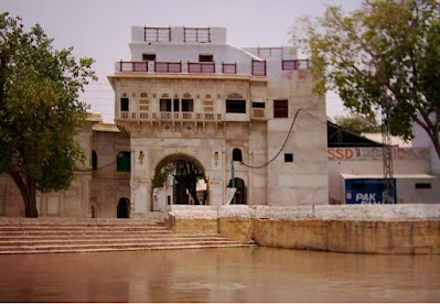 Sadh Belo Temple Entrance on the Indus River Sadh Belo temple entrance with arched gateway and riverside steps in Sukkur, Pakistan" Title: "Sadh Belo Temple Entrance on the Indus River