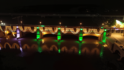 Night view of Sukkur Barrage decorated with green and white string lights draping the arches, green highlights on pillars, and reflections in the Indus River during Jashn e Azadi festivities in Sukkur, Pakistan.