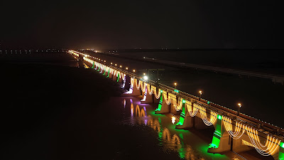 Evening scene of visitors capturing photos at the illuminated Sukkur Barrage, decorated with green and white lights for Jashn e Azadi, featuring river reflections and a magical cultural celebration vibe.