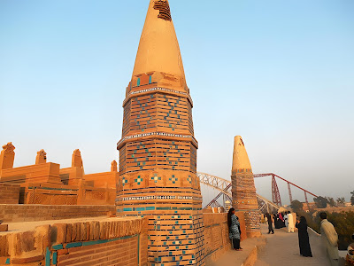 Pinnacles of Sateen Jo Aastan: Tiled Towers and Bridge Views in Rohri, Pakistan Conical tiled pinnacles at Sateen Jo Aastan with visitors and Indus River bridges in background, Rohri, Sindh, Pakistan