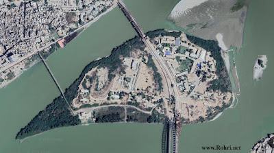 Bukkur Island – بکر جو جزيرو: Fortified Heart of Rohri & Sukkur Satellite view of Bukkur Island (بکر جو جزيرو) in the Indus River, located between Rohri and Sukkur in Sindh, Pakistan. The image shows dense urban structures, bridges connecting to the mainland, and the historic fort’s central position in Sukkur district.