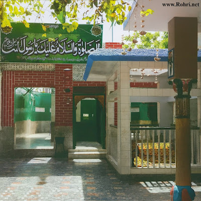 Dargah Hajna Shah Huzoori β vibrant shrine architecture and tomb pavilion in Rohri, Sukkur Dargah Hajna Shah Huzoori in Rohri, Sukkur β vibrant shrine entrance with red bricks, green doors, turquoise tiles, golden tomb cloth, and multicolored stone flooring under tree shade