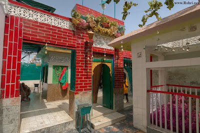 Dargah Hajna Shah Huzoori β vibrant shrine architecture and tomb pavilion in Rohri, Sukkur Dargah Hajna Shah Huzoori in Rohri, Sukkur β vibrant shrine entrance with red bricks, green doors, turquoise tiles, golden tomb cloth, and multicolored stone flooring under tree shade