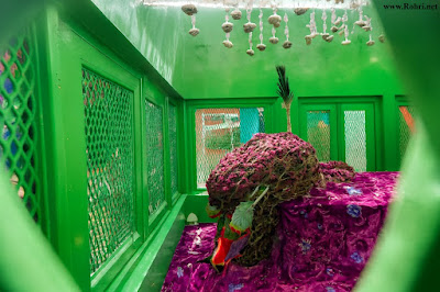 Sacred floral shrine in Sukkur β spiritual reverence and heritage Shrine interior in Sukkur with dried roses, purple embroidered cloth, green mesh windows, and hanging shell ornaments