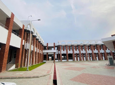 Educational Campus Architecture – Red Brick Courtyard with Arched Designs in Sindh Modern educational campus courtyard with red brick buildings, white decorative arches, patterned tile flooring, and green grass patches under a bright sky.