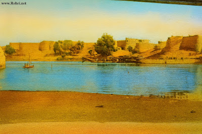 Riverside Fort – Ancient Walls and Bridge Over the Indus Colorized historical image of ancient fortifications along the Indus River near Sukkur, Sindh. The scene includes weathered bastions, a steel truss bridge, small boats, and a sandy riverbank—capturing early 20th-century architecture and riverine life.