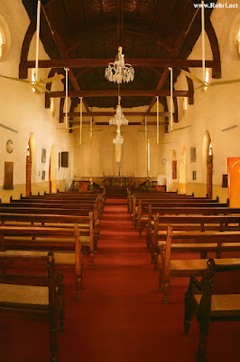 Saint Saviour’s Church Sukkur Interior – Historic Wooden Architecture and Red Carpet Aisle Interior view of Saint Saviour’s Church in Sukkur, featuring wooden pews, red carpet aisle, arched ceiling with chandeliers and fans, and altar under natural daylight