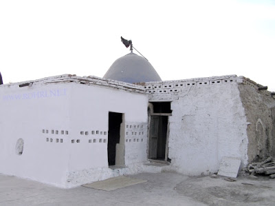 Traditional Dome Structure of Shah Maqsood Site – Rohri Heritage A rustic whitewashed building with a dome and black flag, part of Shah Maqsood’s heritage site in Rohri, Sindh, showcasing traditional architecture with mud-brick walls and aged textures.