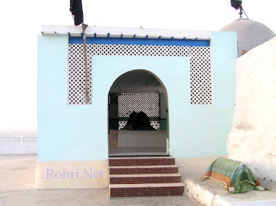 Shah Maqsood Shrine Rohri – Sindh’s Sacred Sufi Heritage Site Exterior view of Shah Maqsood’s shrine in Rohri, Sindh – featuring blue walls, red steps, and black flag