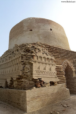 Shaikh Laloo Pir Shrine – Weathered Brick Dome and Ornate Facade in Rohri, Sindh Ancient brick structure of Shaikh Laloo Pir Shrine in Rohri, Sindh, featuring a cylindrical dome and intricately carved lower facade with decorative arches and geometric patterns, partially damaged and under inspection.