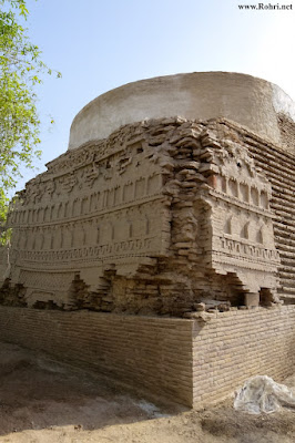 Shaikh Laloo Pir Shrine – Restoration of Ancient Brick Dome in Rohri, Sindh Restoration of Shaikh Laloo Pir Shrine in Rohri, Sindh, showing scaffolding, workers, and intricate brickwork with arched niches and geometric patterns beneath a weathered dome, surrounded by bricks and greenery under clear skies.